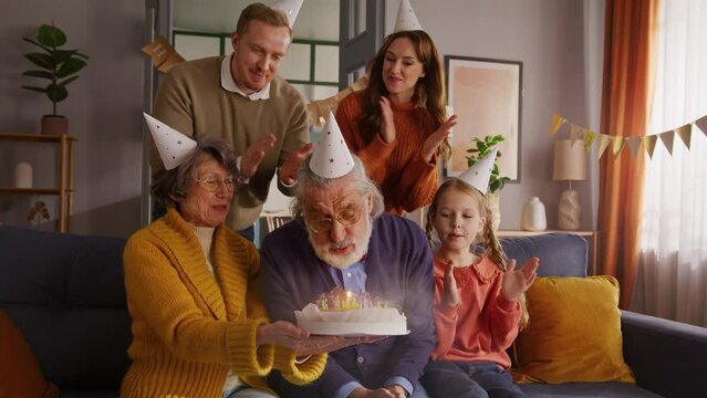 Delighted family waiting for grey old man blowing candles