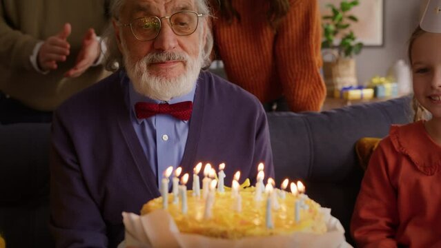 Elderly male blowing on burning candles on birthday cake