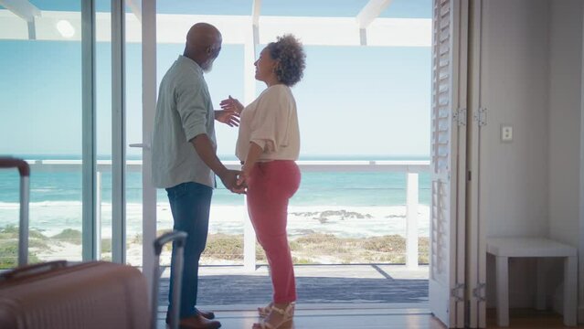 Low angle shot of mature couple with luggage arriving for holiday in beach front property overlooking ocean holding hands together - shot in slow motion