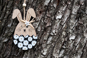 Happy Easter greeting card with place for text. Easter decor. Decorative wooden toy Easter bunny on background of tree bark.