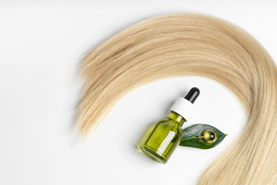 A lock of silky blonde hair elegantly loops around a green dropper bottle with a natural citrus extract and CBD oil, complemented by yellow capsules and a metallic facial roller