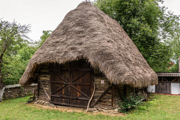 Fototapeta na wymiar Wooden barn with thatched roof in open air museum Oas Village in Negresti-Oas town, Romania
