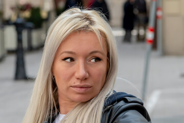 A beautiful woman 35-40 years old sits and looks away on a blurred city background.