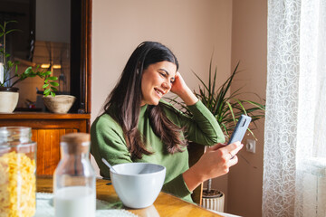 A young girl or woman is using her laptop to talk to friends or listen to music or taking selfie while eating breakfast	
