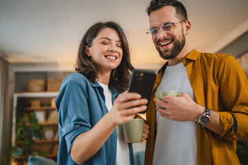 Adult couple man and woman husband wife have a cup of coffee use mobile phone search internet social network happy smile - obrazy, fototapety, plakaty