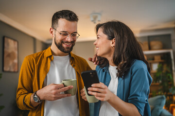 Adult couple man and woman husband wife have a cup of coffee use mobile phone search internet...