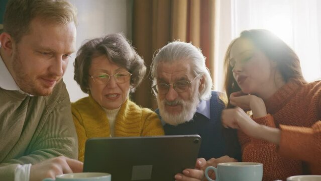 Couple showing screen of tablet to elderly female and male