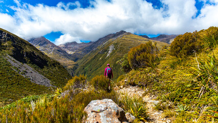 hiker girl with a backpack walking on a trail surrounded with mountains - otira valley track in arthur's pass national park, canterbury, new zealand south island © Lens Down Under