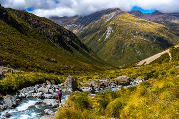 backpacker standing on the rocks next to crystal clear otira river, enjoying the panorama of otira...