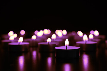 Burning violet candle on black background, closeup. Funeral attributes