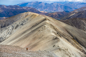 hiker girl walking down a very steep rocky hill from the summit of castle hill peak, torlesse tussocklands national park, new zealand south island