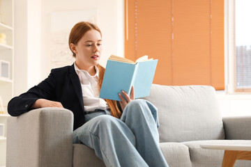 Young businesswoman reading book at home after long working day