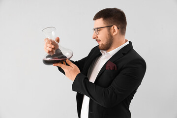 Young sommelier with decanter of red wine on grey background