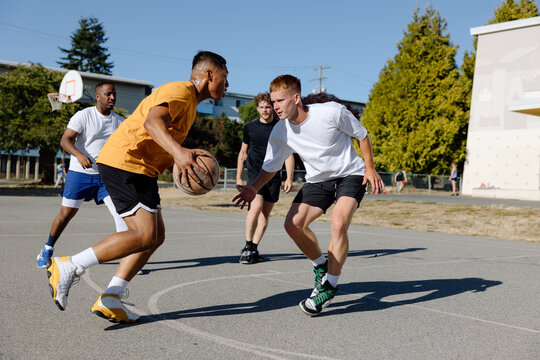 A group of friends playing basketball together outside in the su