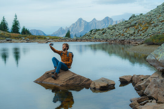 Man sitting at scenic lake at using smartphone to take a picture