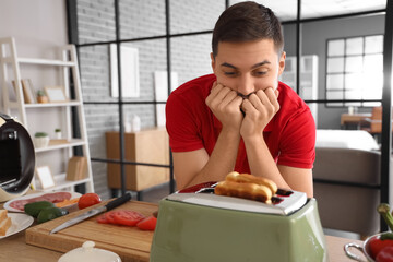 Impatient young man waiting for toasts in toaster at home
