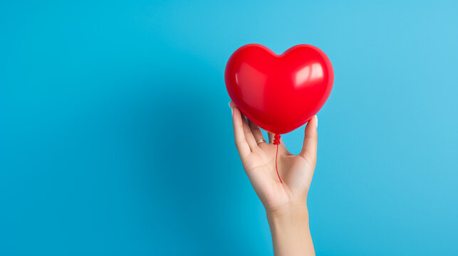 A hand holding a red heart shaped balloon, blue background, photo