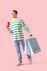 Young man with gift voucher and shopping bags walking on pink background