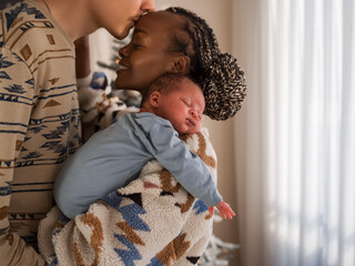 Loving husband kissing wife holding baby at home