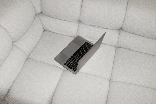 Silver laptop lying on a grey couch/sofa with hard direct flashlight