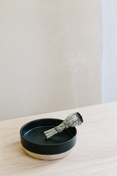 Smoking sage stick in a ceramic bowl.