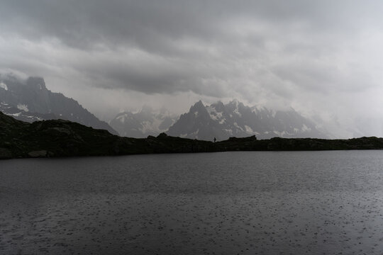 Tiny traveler figure near Lac De Cheserys lake at rain