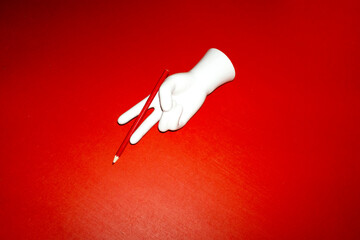 Porcelain hand holding a red pencil with hard direct flashlight