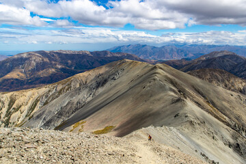 hiker girl walking down the steep and narrow rocky trail from castle hill peak in southern alps, canterbury, new zealand south island