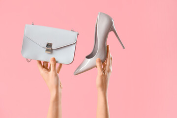 Female hands with stylish women's bag and high heels on pink background
