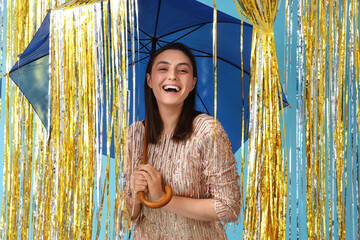 Young woman with umbrella and tinsel on blue background