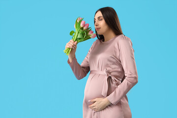 Young pregnant woman smelling tulips on blue background