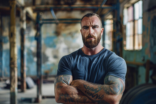 A man with a beard and tattoos on his arms stands with his arms crossed