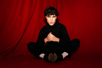 Young man in stylish clothes sitting in red studio
