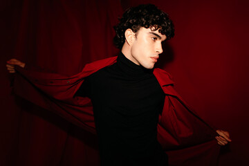 Pensive young curly haired man in black dress displaying red jacket