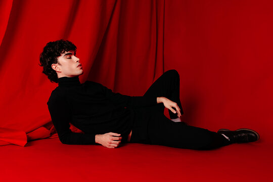 Stylish young model lying on red floor in studio