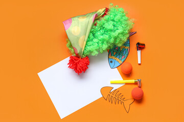 Blank card with paper fishes, clown wig and party whistles on orange background. April Fools Day...