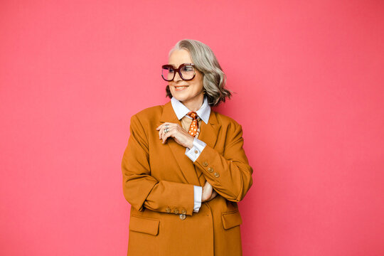 Cheerful senior woman in yellow jacket on pink studio background 