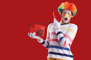 Portrait of surprised clown with retro telephone on red background. April Fool's day celebration