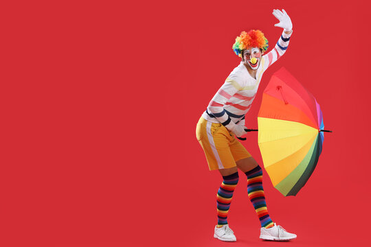 Portrait of clown with colorful umbrella on red background. April Fool's day celebration