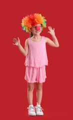 Cute little girl with colorful clown wig on red background. April Fool's Day celebration
