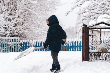 Kid Boy clearing snowy path in a suburban countryside house yard