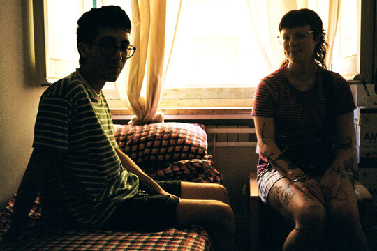 Backlit silhouettes of young Gen-Z couple sitting on bed in bedroom