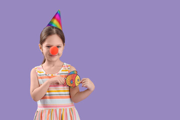 Cute little girl with clown nose, party hat and paper fish on lilac background. April Fool's Day celebration