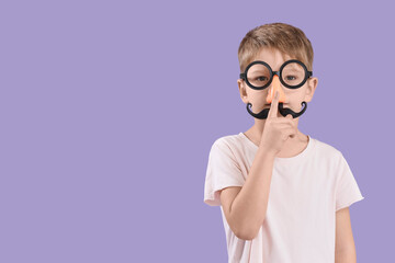 Cute little boy in funny disguise showing silence gesture on lilac background. April Fool's Day...