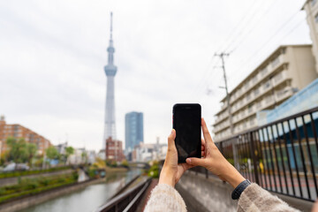Asian woman hand using mobile phone during walking by the river in Tokyo city, Japan with cityscape...