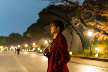 Portrait of Young Asian man holding umbrella walking city street crosswalk with night lights in...