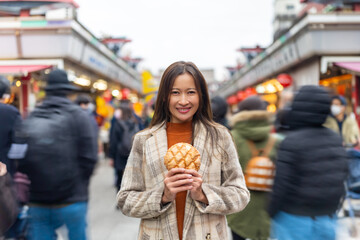 Happy Asian woman eating Japanese sweet bread during travel at Asakusa district, Tokyo, Japan....