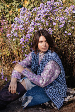 Woman sitting in blooming garden with bushy aster flowers
