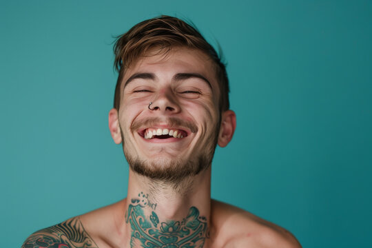 A shirtless man with a tattoo on his neck laughs with his eyes closed
