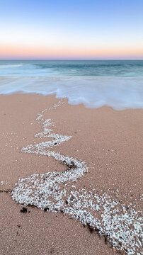Coral bits on sandy beach and long-exposed ocean wave at sunset